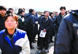 手拿“钱少”牌子的男子向厂区内张望。昨日，因不满协议离职，400余位松下员工堵在厂门口讨说法。